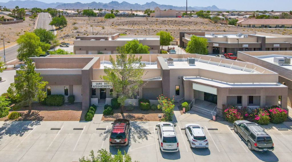 Exterior view of primary care clinic in Bullhead City, Arizona, with parking lot, desert landscape, and nearby offices.