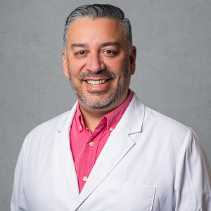 Erik P Munoz, experienced primary care provider at Optima Medical in Prescott, Arizona, wearing a white coat and red shirt.
