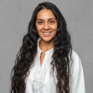 Lirio Miller, healthcare provider at Optima Medical in Tucson, Arizona, smiling in a white coat with long wavy hair.