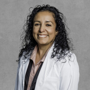 Alma A. Tinoco, primary care provider at Optima Medical in Surprise, Arizona, wearing a white coat and smiling against a gray background.