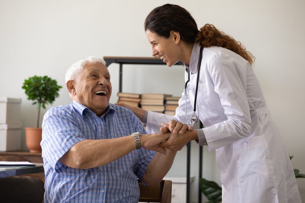 Friendly Female Doctor Holding Hands With Smiling Senior Male Patient at Optima Medical Primary Care Clinic in Arrowhead, Glendale, AZ.