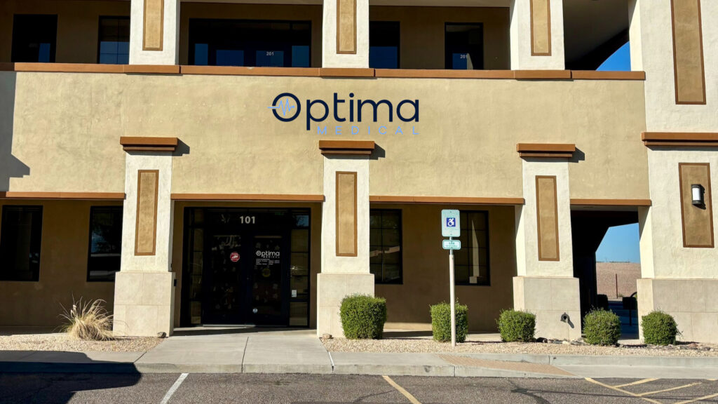 Exterior of Optima Medical North Gilbert clinic with building entrance, accessible parking, and Optima Medical signage on the front of the building.