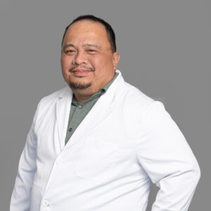 Rey Roferos, healthcare provider at Optima Medical in South Bullhead City, Arizona, wearing a white medical coat and smiling.