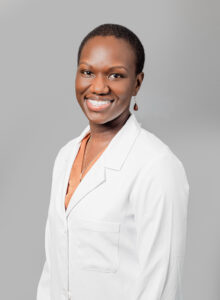 Smiling Optima Medical provider wearing a white lab coat against a neutral gray background